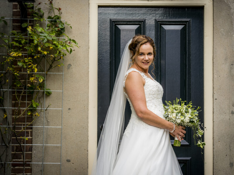 Bruid kijkt in camera voor deur. Fotograaf Karin Keesmaat van Kijk-Kunst fotografie