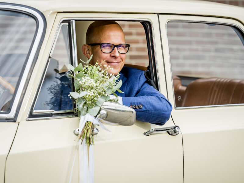 Bruidegom glimlacht vanuit auto. Fotograaf Karin Keesmaat van Kijk-Kunst fotografie