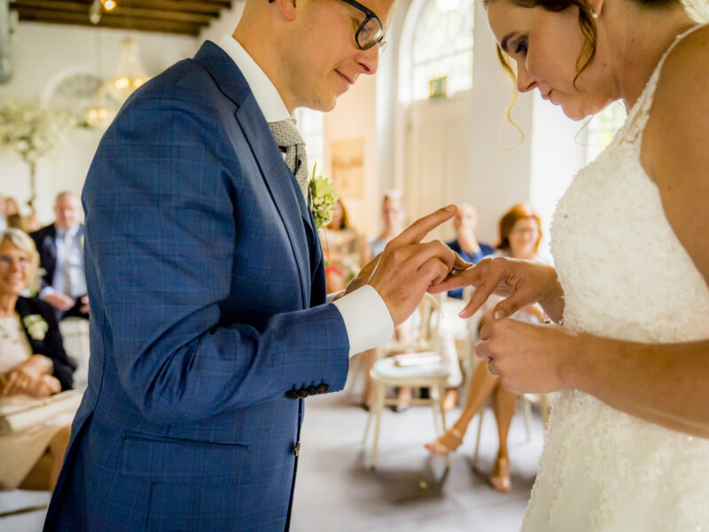 Bruidegom schuift ring om vinger bruid. Fotograaf Karin Keesmaat van Kijk-Kunst fotografie